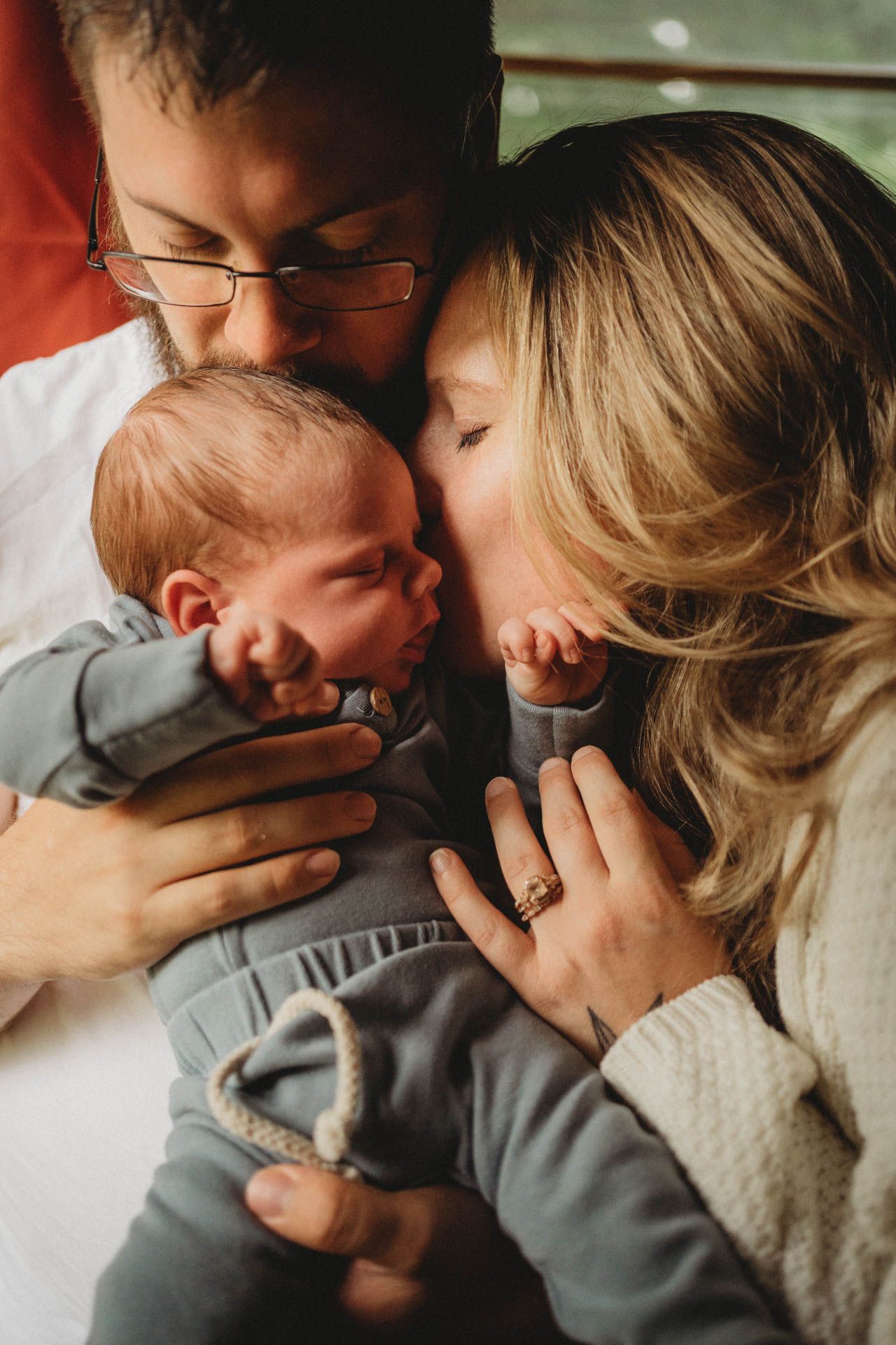 Intimate family moment with newborn baby being held and kissed by parents.