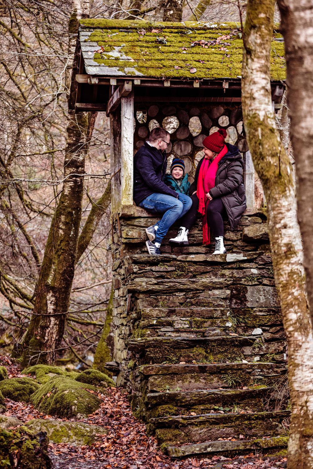 Group sitting together in a moss-covered wooden shelter on stone steps in the forest.