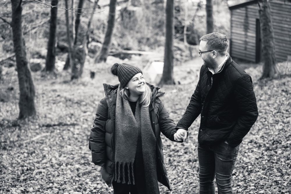 Intimate black and white moment captured of couple walking through autumn woods.