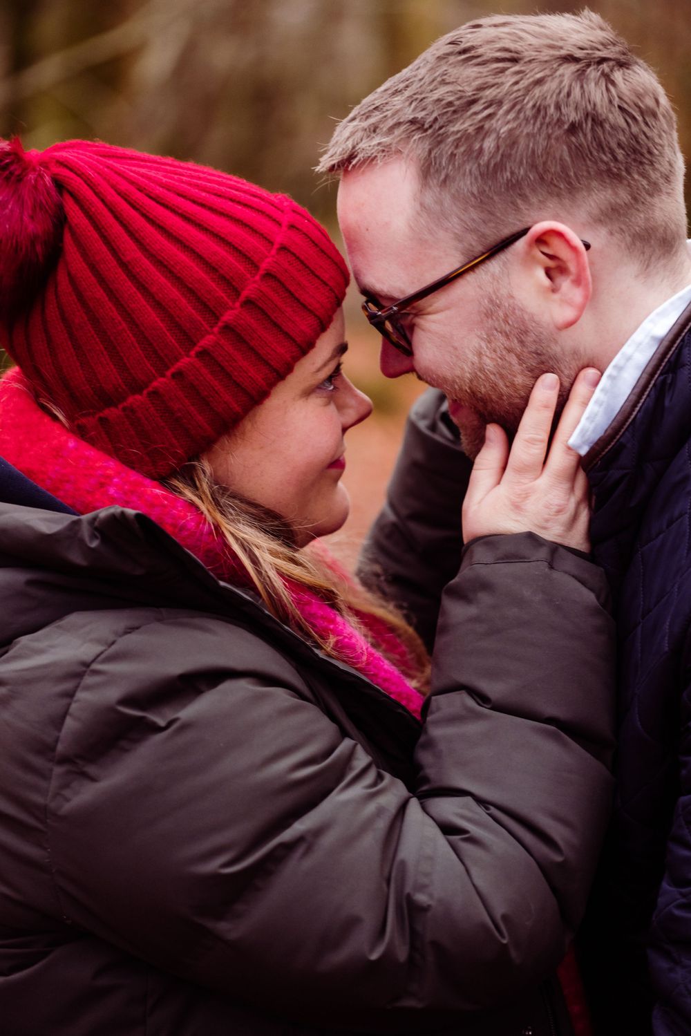 An intimate moment between a couple in winter attire against an autumn forest backdrop.
