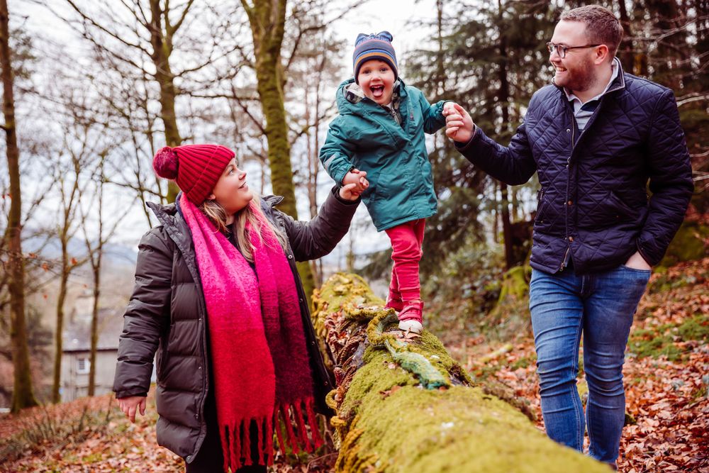 Family enjoying autumn day together balancing on fallen log in forest.