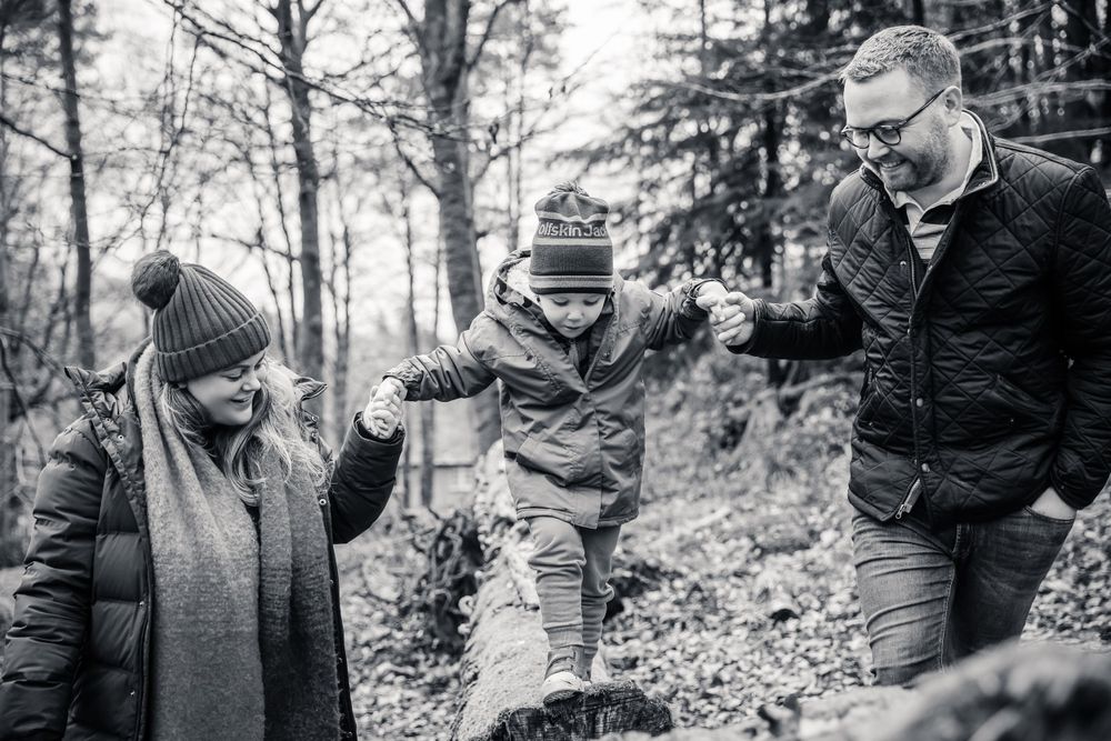 Black and white photo of family enjoying playful moment on forest path.