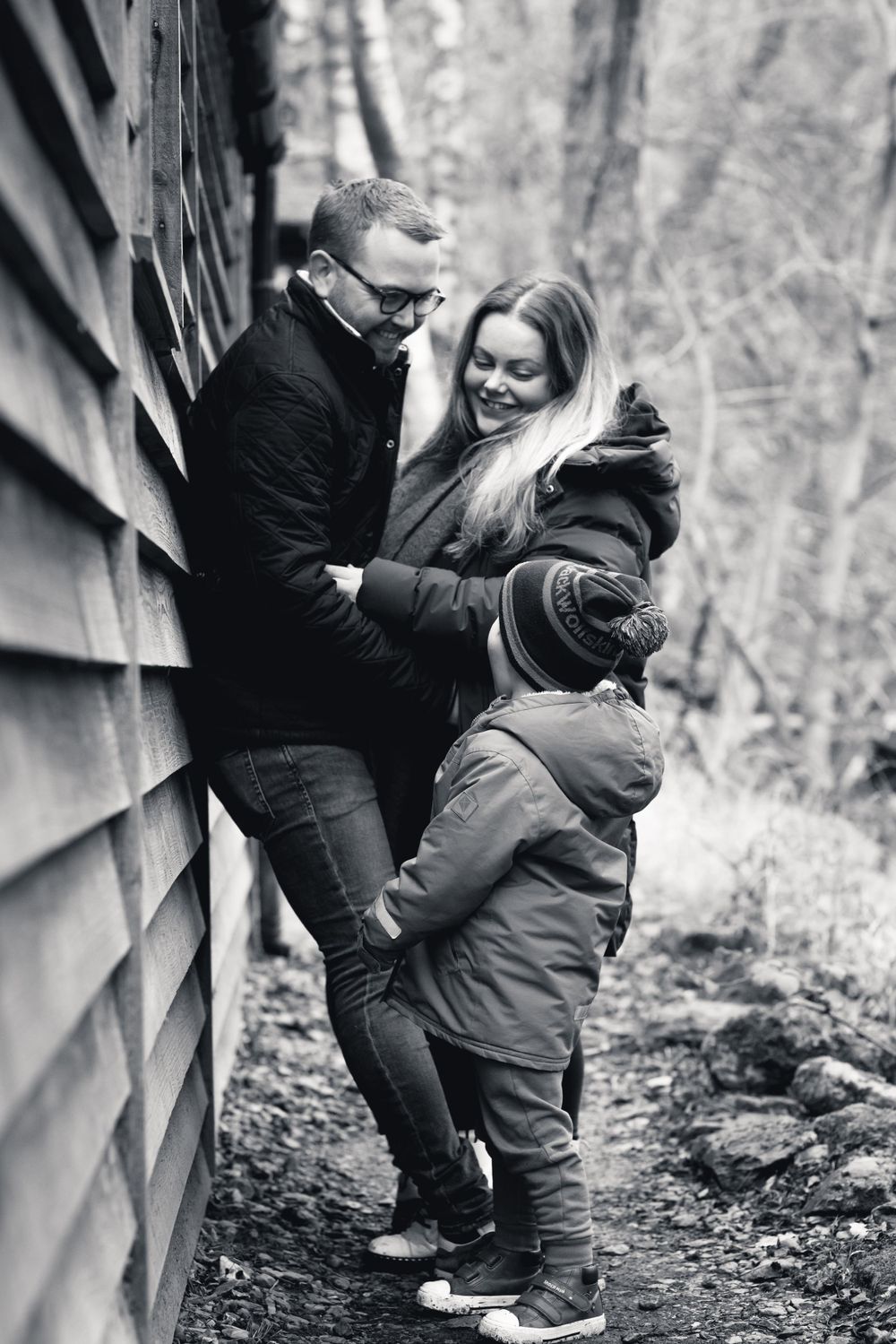 Black and white family portrait against rustic wooden wall in nature setting.