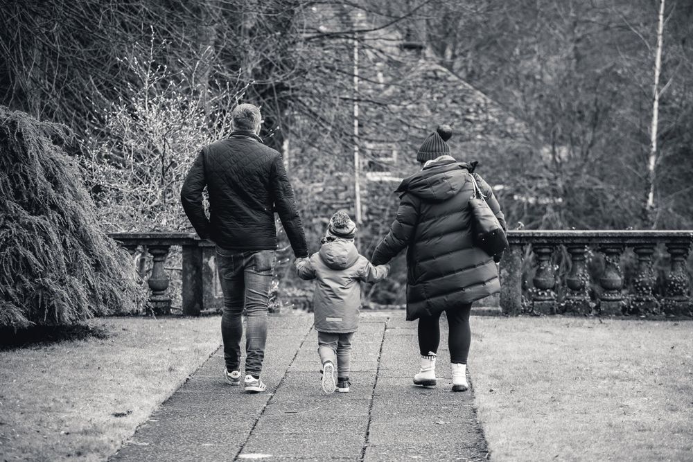Three people walking hand in hand along a stone pathway in black and white.