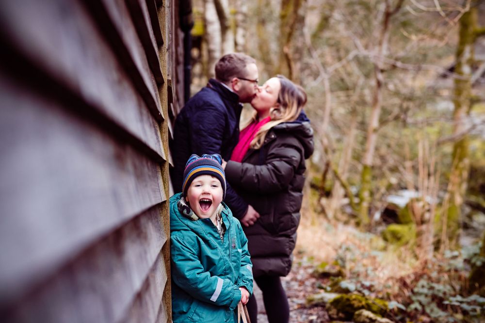 Family moment captured against wooden wall with turquoise-coated child in foreground.