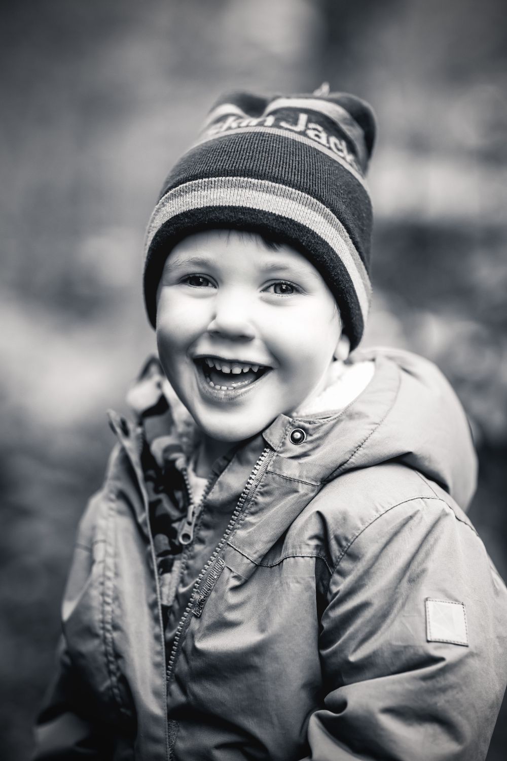 Cheerful young child wearing a winter hat and coat smiles brightly in black and white portrait.