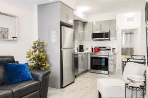 Modern apartment interior with gray couch, blue accents, and stainless steel kitchen appliances.