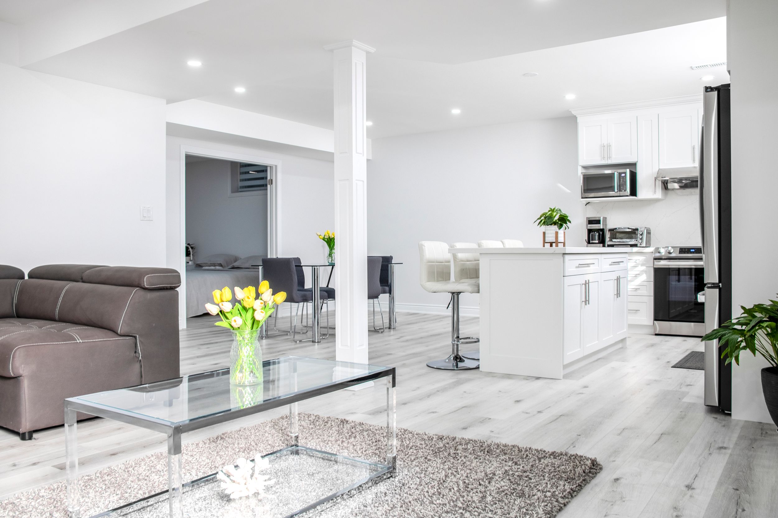 Open concept basement with white walls, grey furniture and glass coffee table.