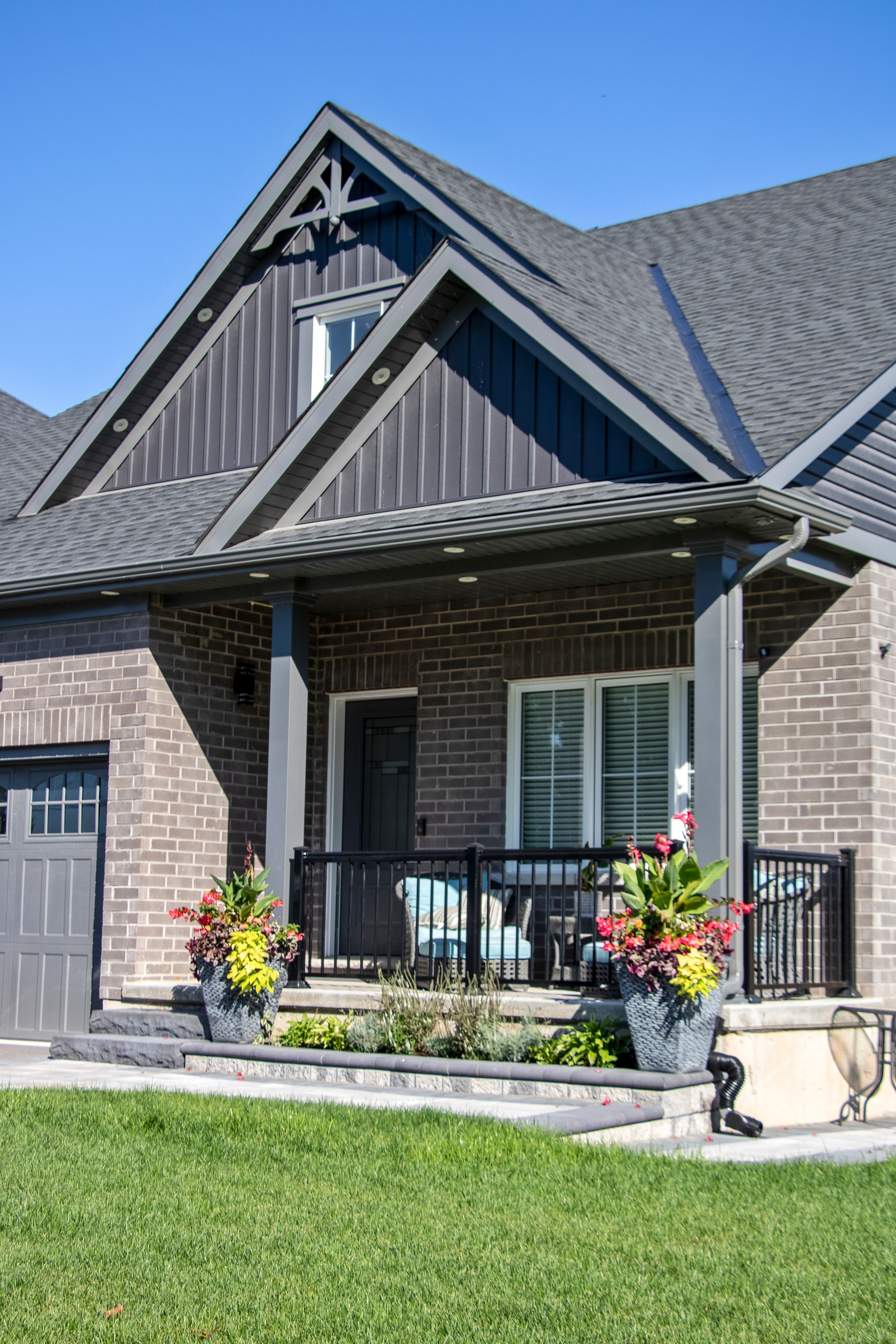 Craftsman style home exterior with grey brick, peaked rooflines and landscaped lawn.