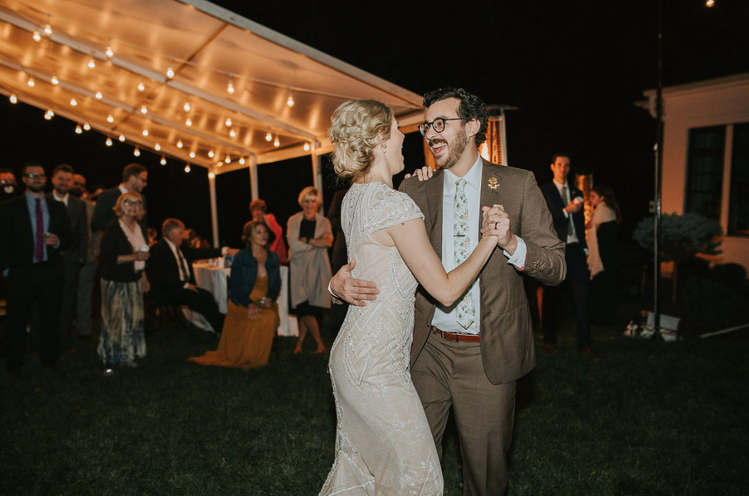 A couple sharing their first dance under string lights at an outdoor evening wedding reception.