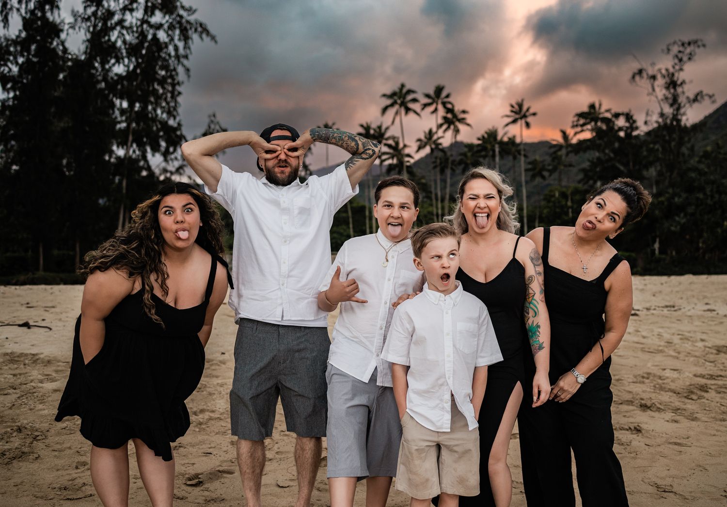 Fun group photo on beach with mountains and palm trees at sunset.