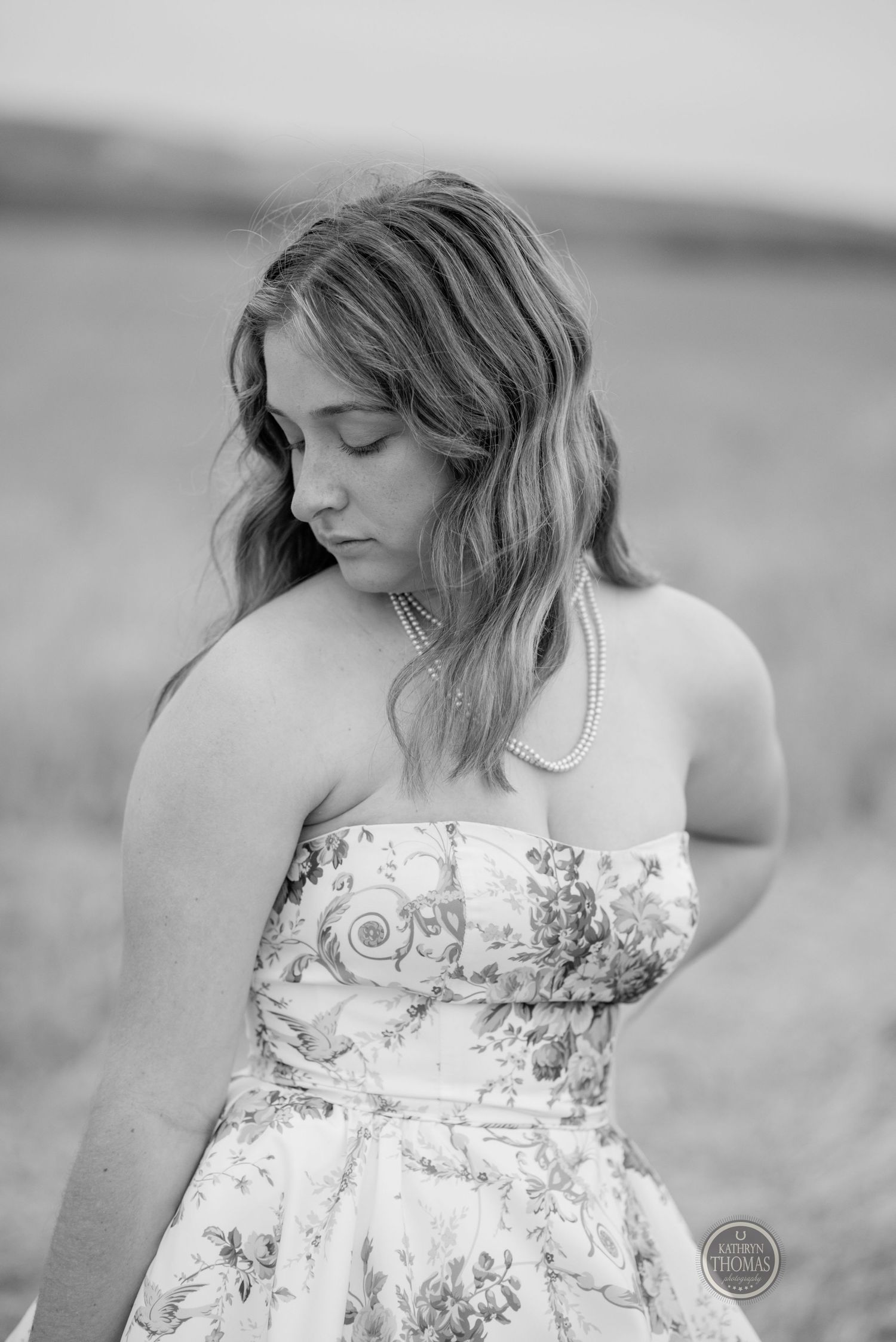 Black and white portrait showing soft profile view in a romantic strapless dress against natural backdrop.