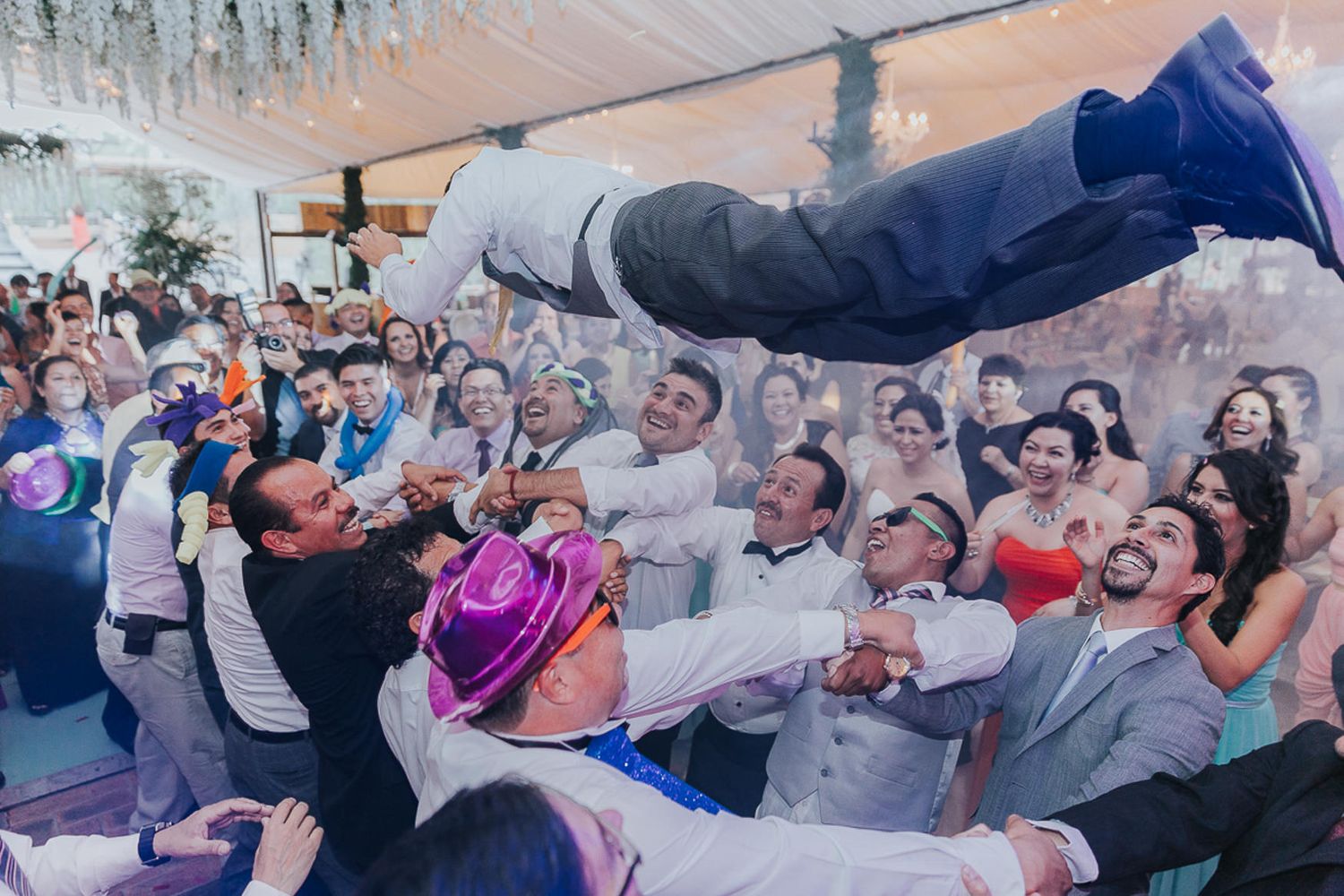 Celebratory crowd lifting and tossing someone during lively wedding reception.