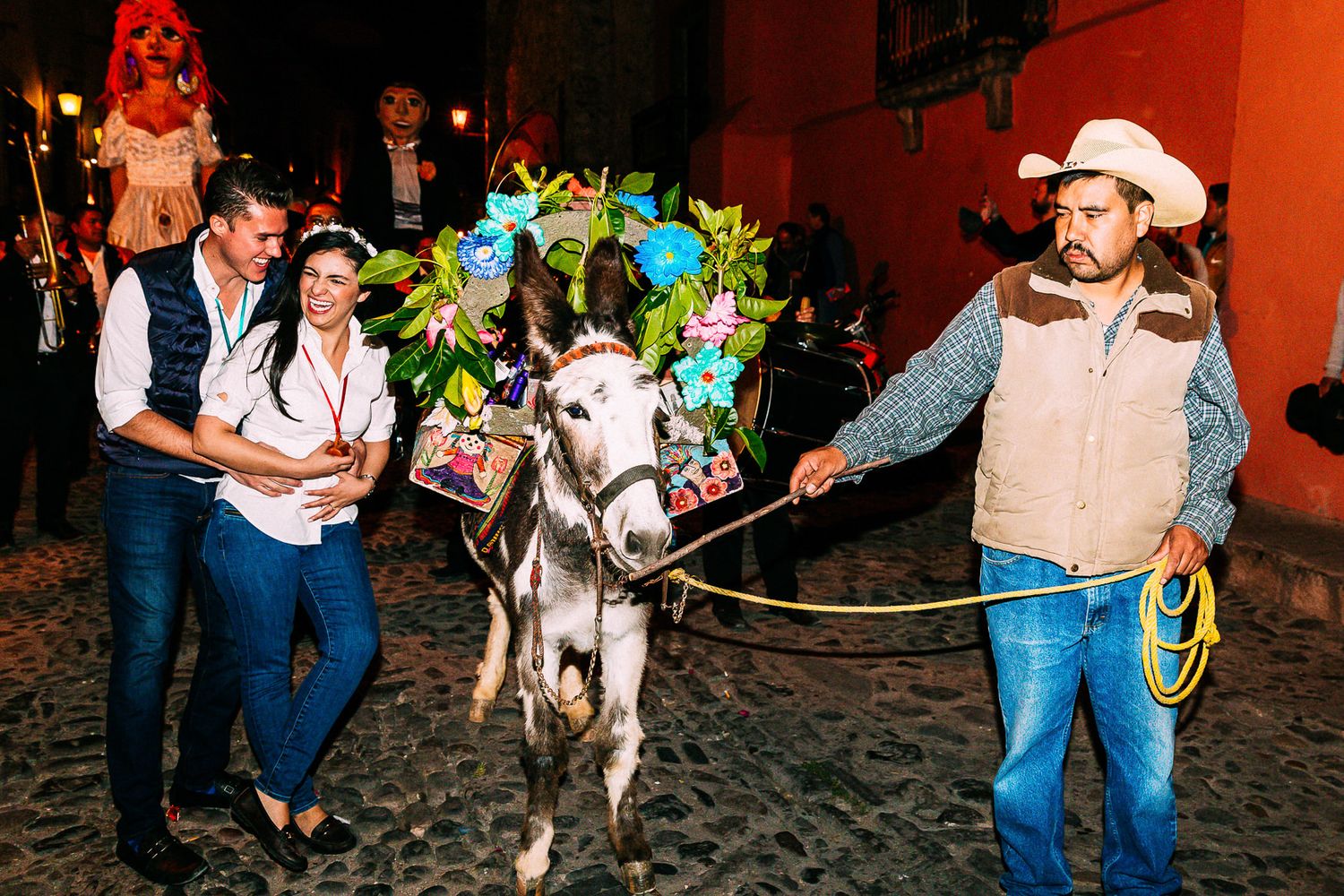 Festive wedding parade featuring decorated donkey with colorful accessories and handlers in western attire.