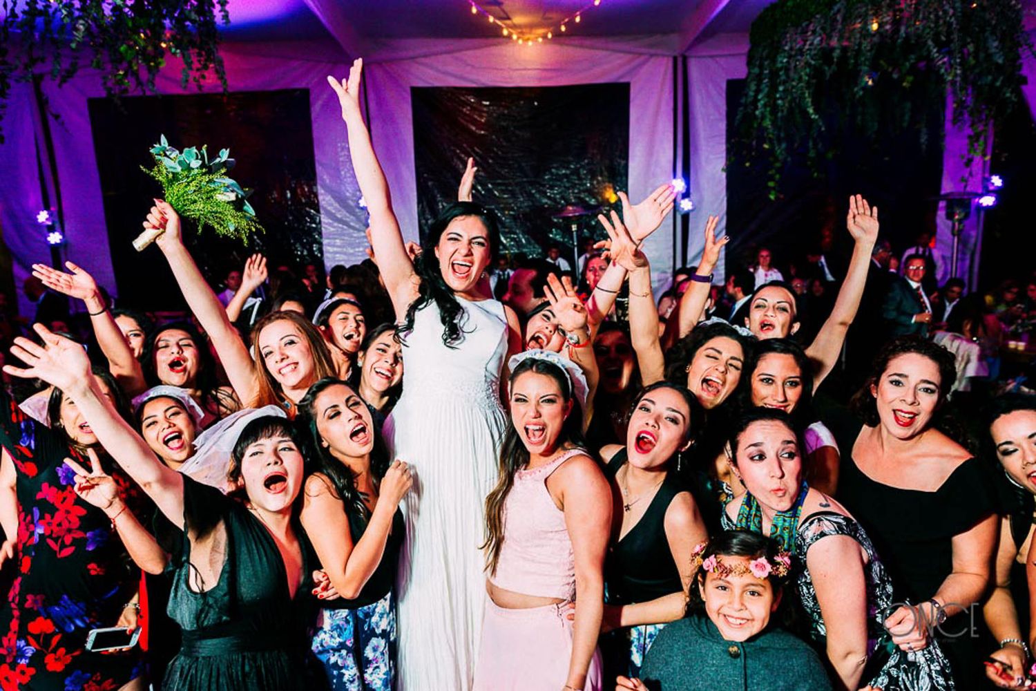 Energetic wedding celebration with crowd of guests cheering and raising hands.