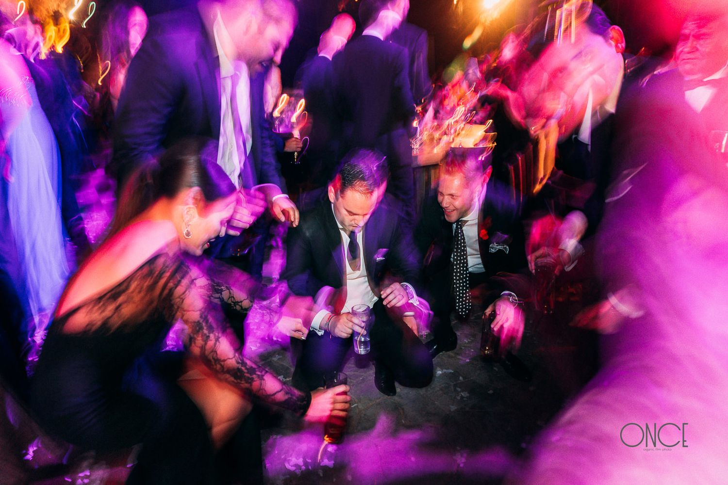 Party guests dance under vibrant pink and purple lighting at a nightclub reception.