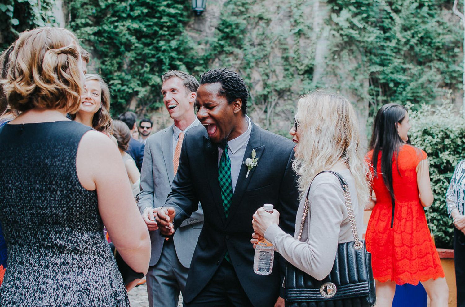 Wedding guests mingle and laugh during an outdoor cocktail reception.