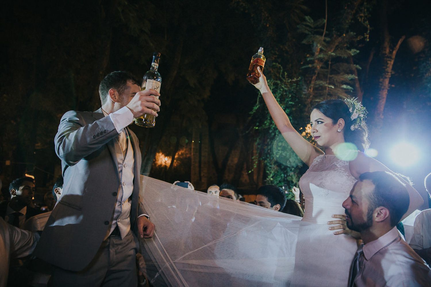 Wedding couple raises their drinks in celebration during outdoor evening reception.