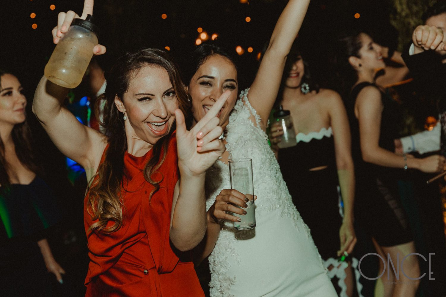 Party guests in formal attire dance and celebrate with drinks on the dance floor.