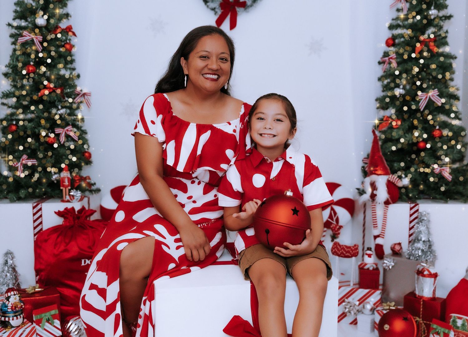 Festive holiday portrait with matching red and white outfits in front of decorated Christmas trees.