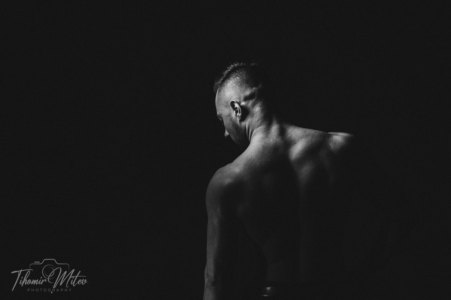 Културист в гръб на черен фон стил low key фотография