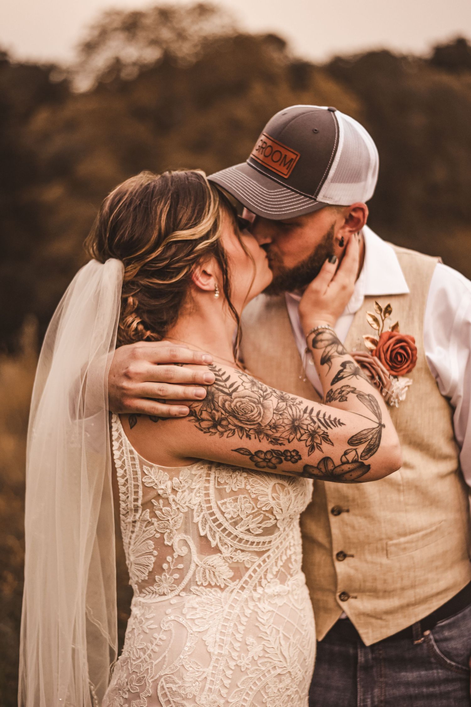 Intimate wedding portrait showing couple embracing with visible tattoos and rustic attire.