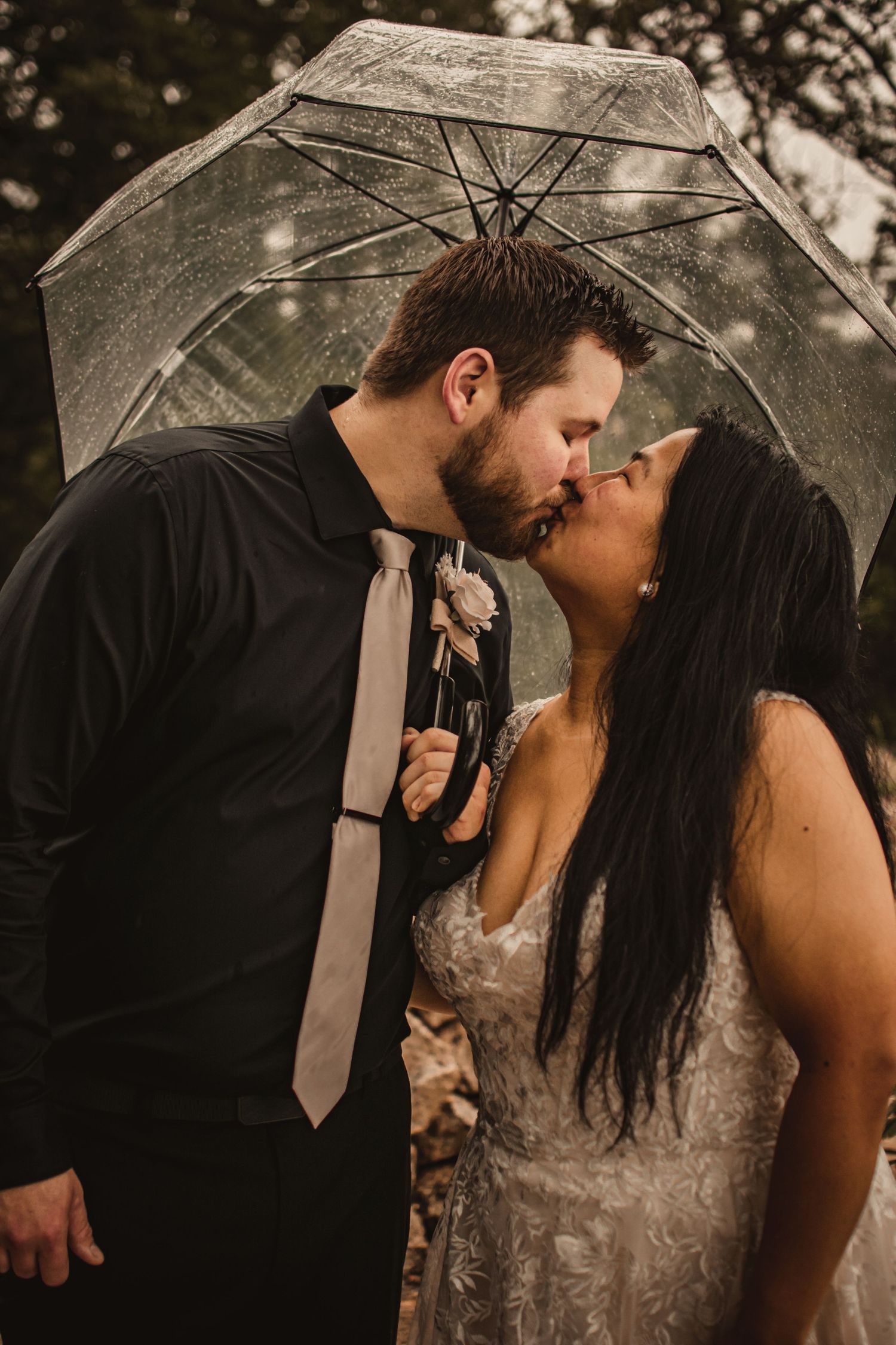 Romantic rainy day wedding portrait under clear umbrella.