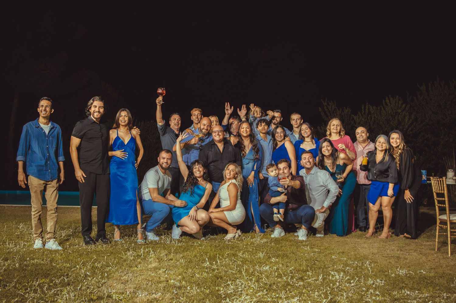 Large group wearing coordinated blue outfits posing together on grass at night.