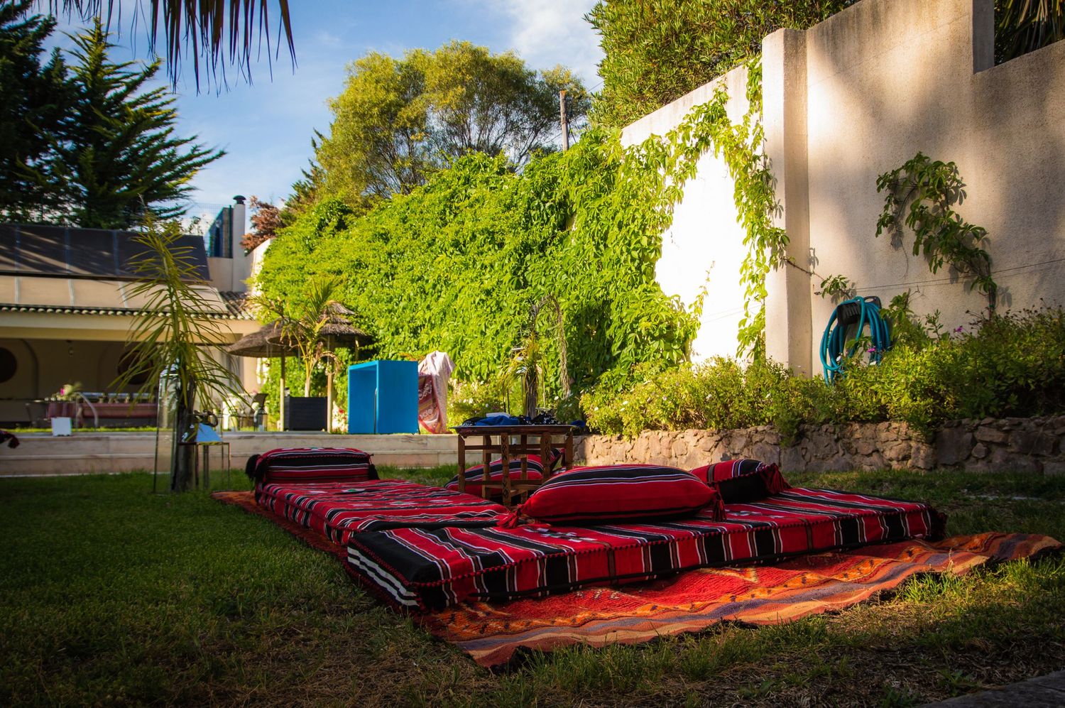 Red cushioned benches line the exterior wall of a Mediterranean-style building with lush greenery.