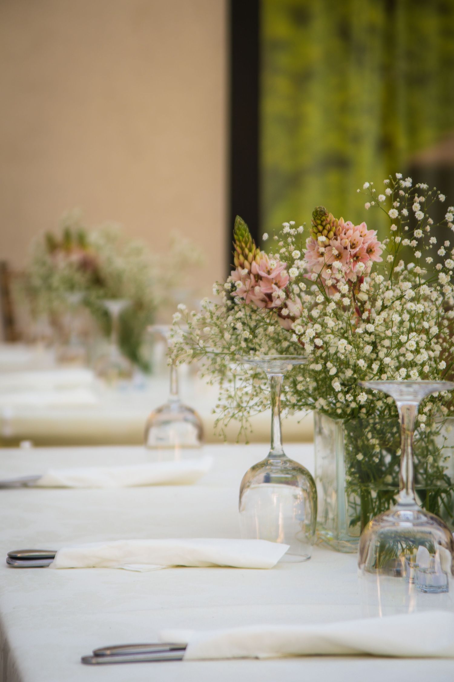 Elegant table settings with delicate baby's breath flowers in glass vases line a white tablecloth.