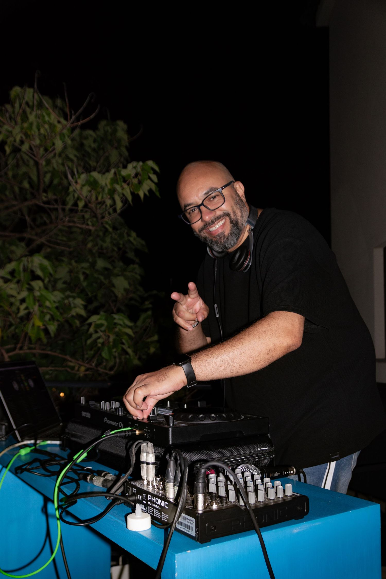 DJ performs at nighttime event with professional audio equipment on blue-lit table.