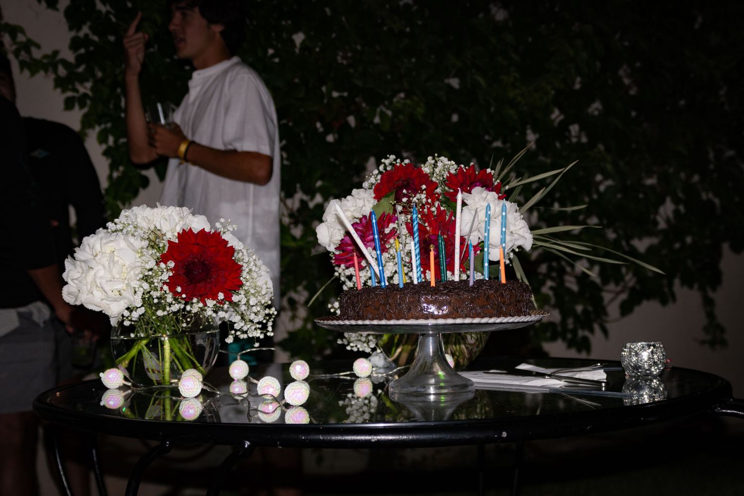 Elegant party decorations with red flowers and candles arranged on dark table at night.
