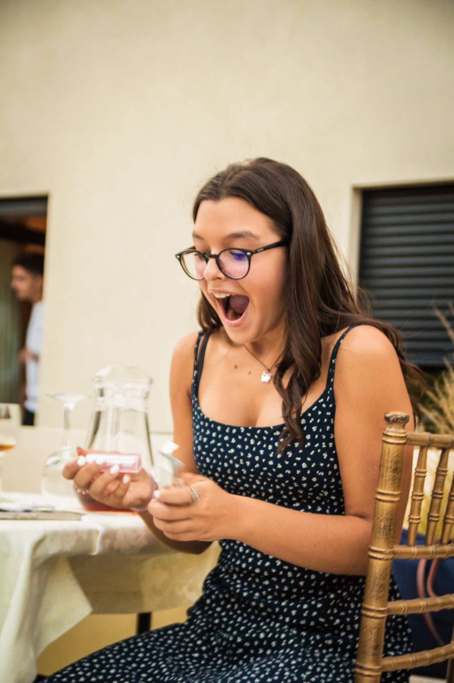 Woman in polka dot dress reacting excitedly while seated at formal dining table.