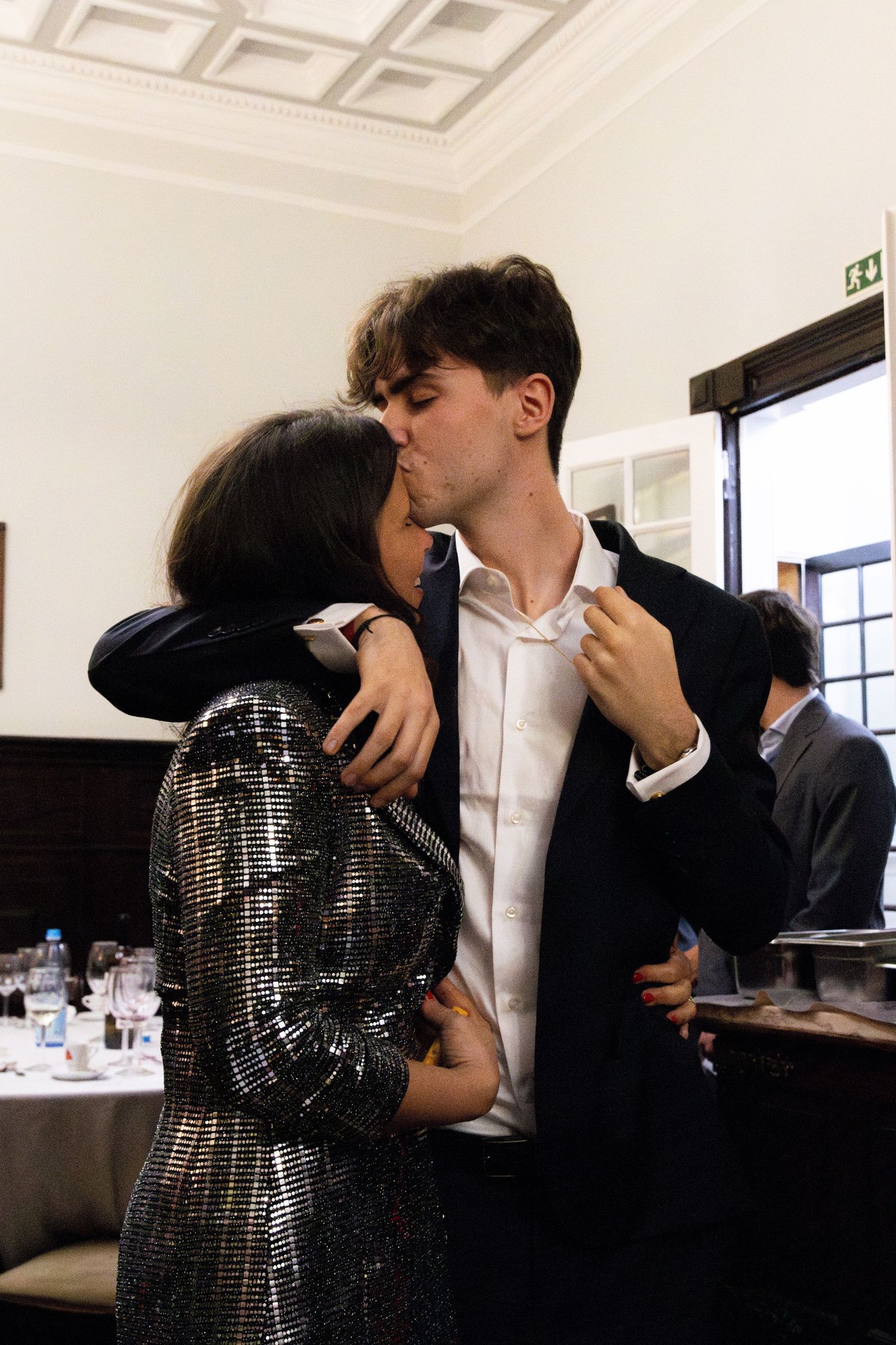 Couple embracing in formal attire inside a modern room with white coffered ceiling.