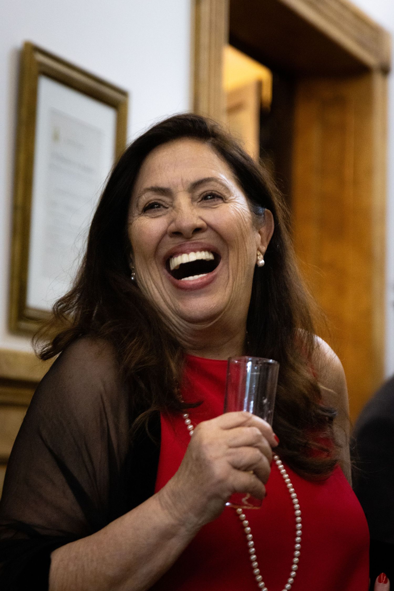 Woman in red sweater and pearls laughing joyfully at a social gathering.