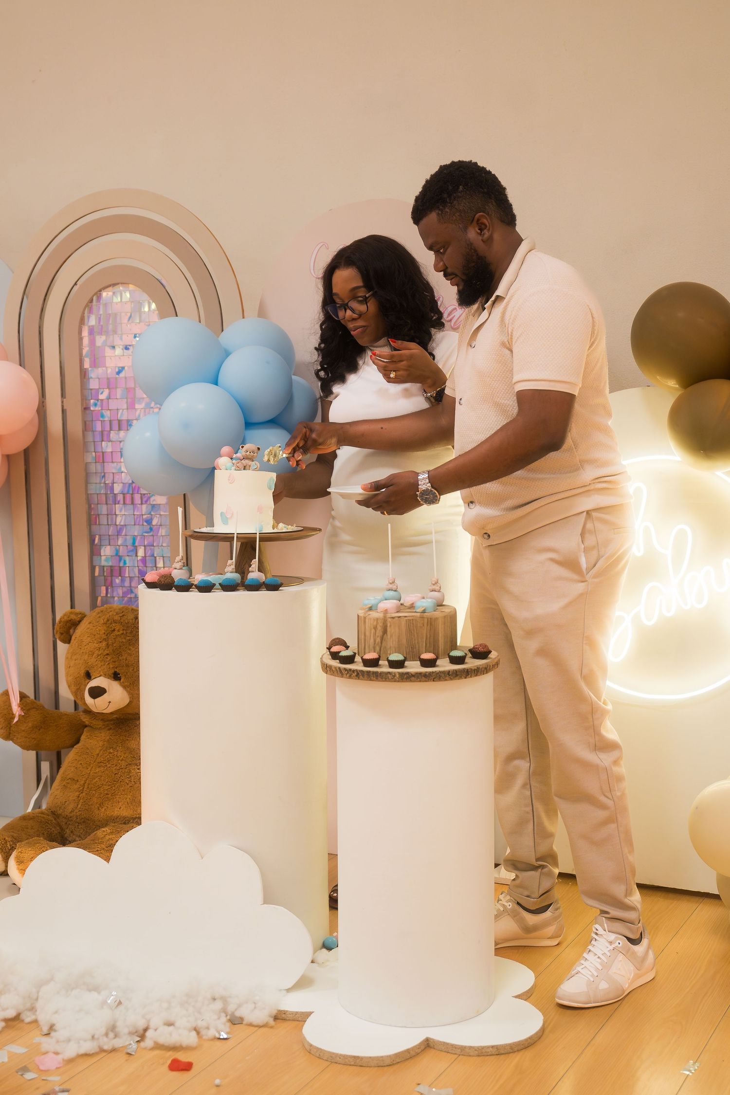 White cake display table with balloon decorations at celebration event.