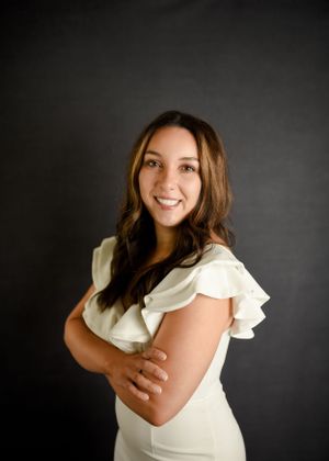 Studio portrait against dark background wearing white ruffled blouse.