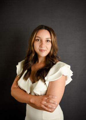 Portrait in white flutter sleeve top against dark studio backdrop.