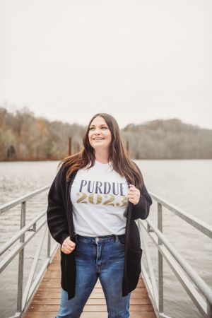 Graduate in Purdue t-shirt posing on wooden dock by lake.