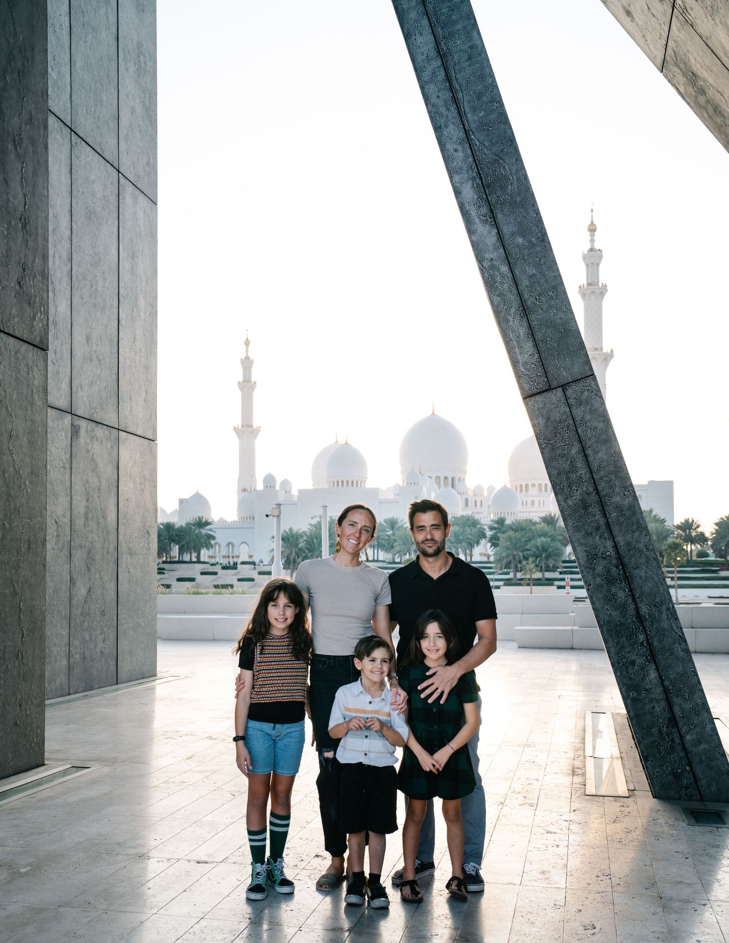 A family stands together at dusk with the Sheikh Zayed Grand Mosque in Abu Dhabi visible in the background.