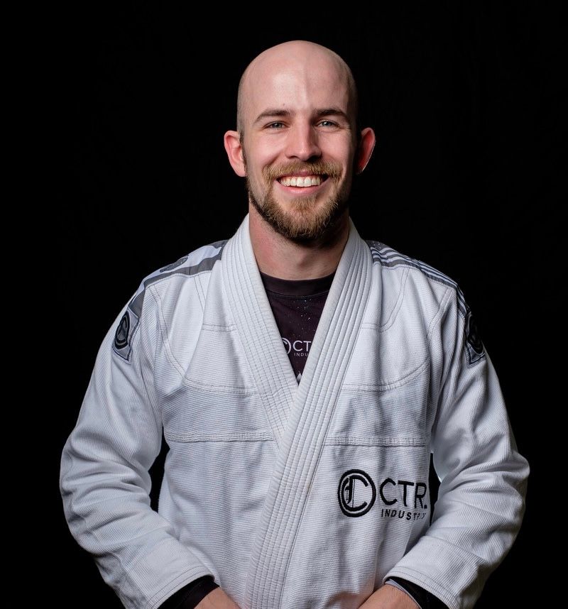 A martial artist in a white gi with CTR patch poses against a dark background.