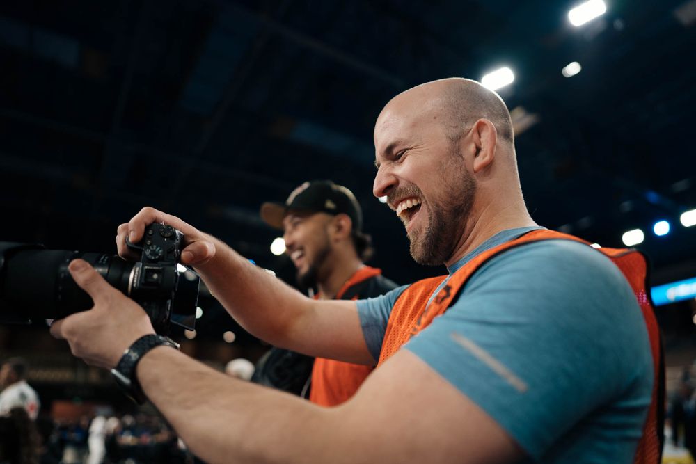 A photographer wearing an orange vest reviews images on two cameras at a sports venue.