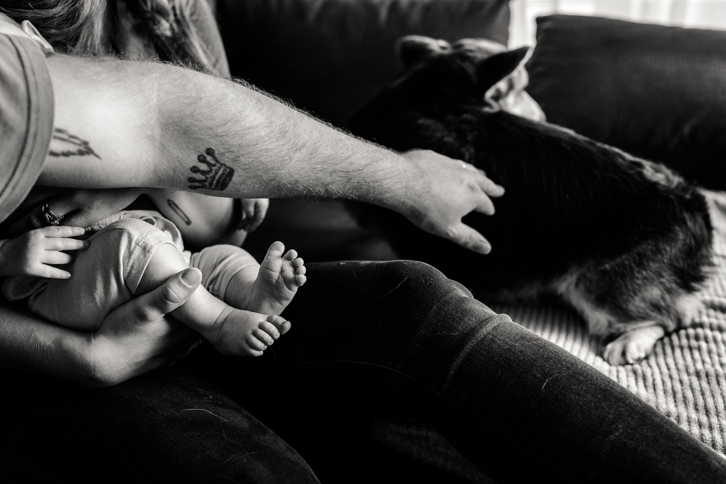 Black and white photo of a baby's feet next to a resting dog on a couch.