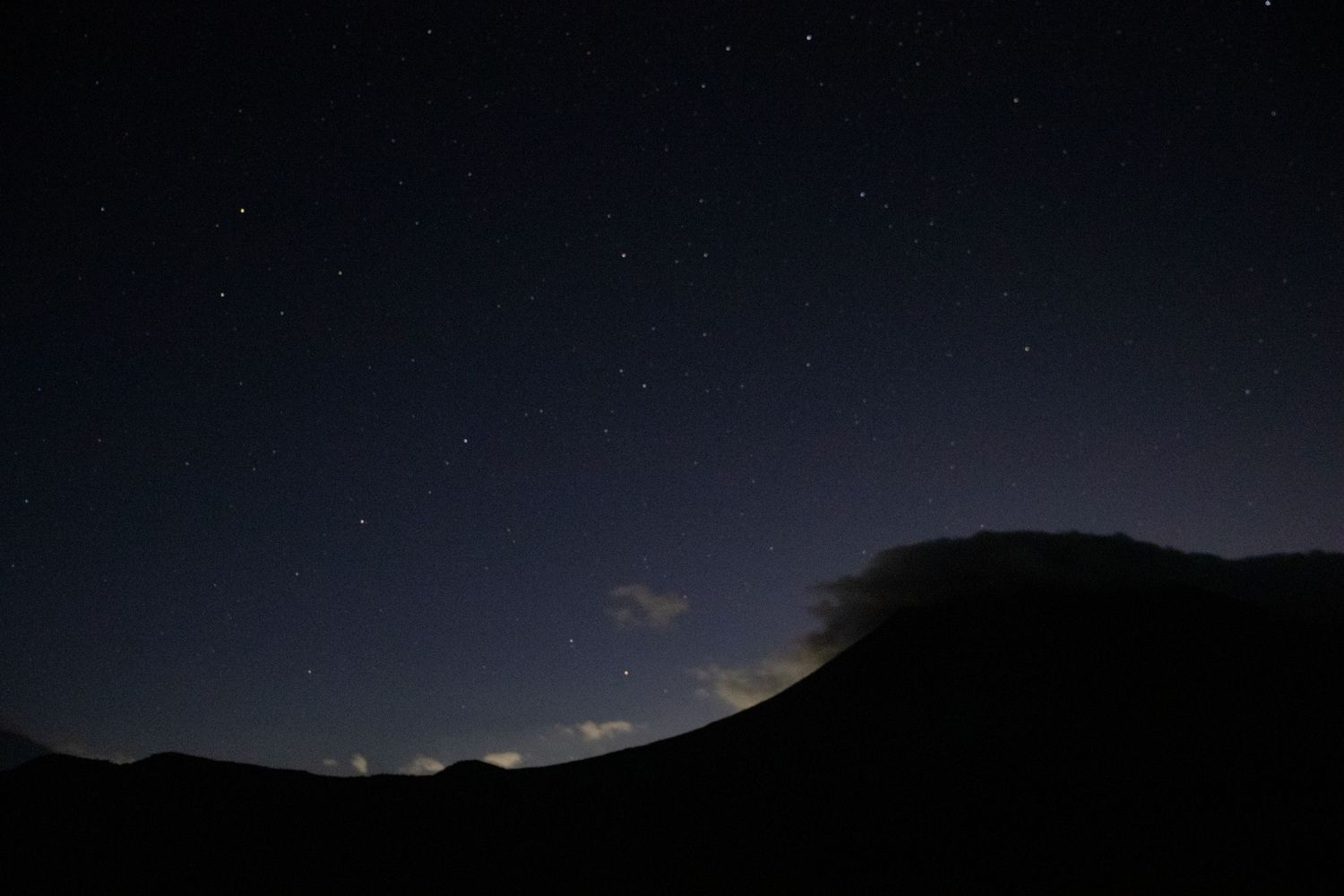 Dark mountain ridges silhouetted against a star-filled night sky with subtle cloud formations.