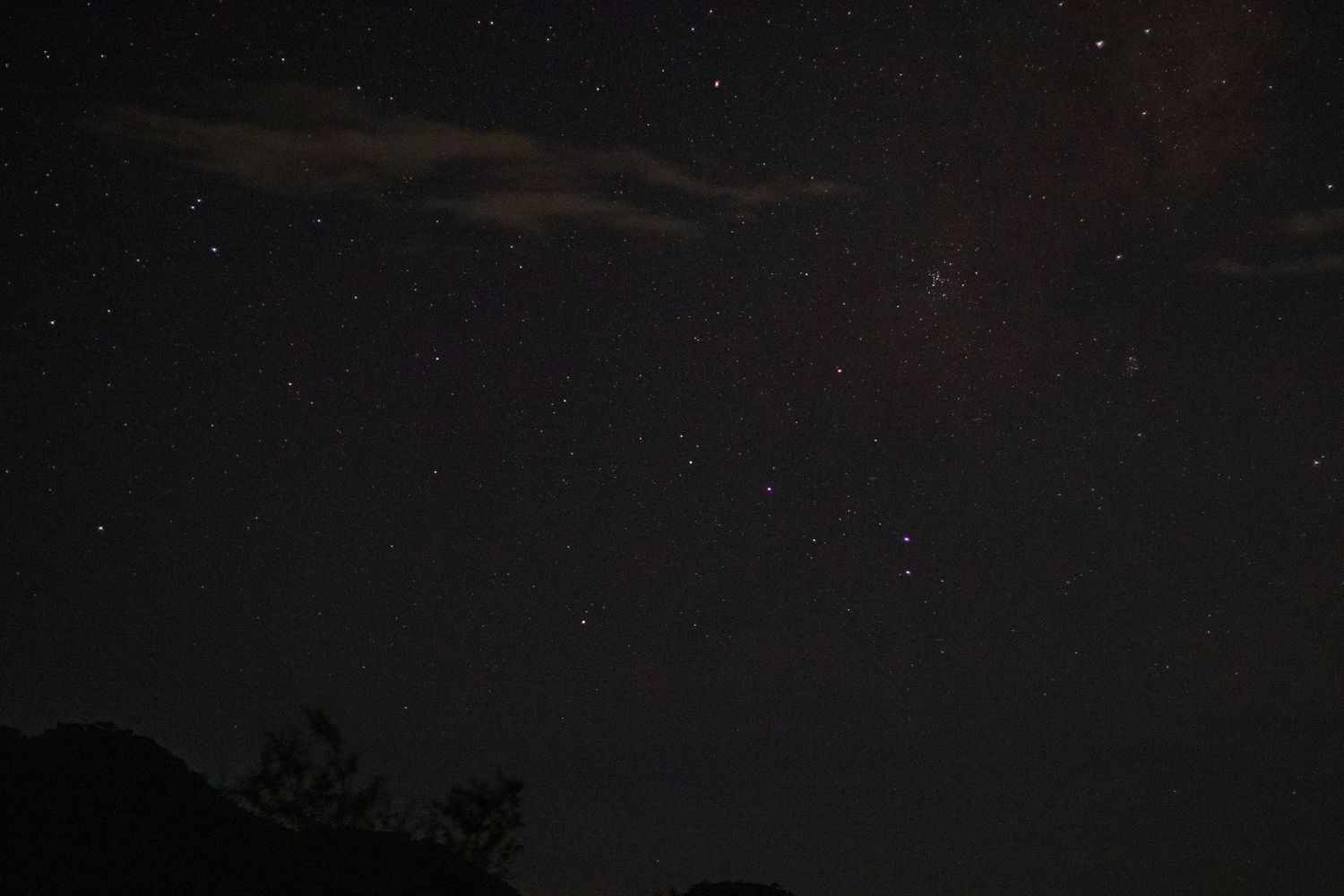 Panoramic view of mountains against a dark starry night sky with scattered clouds.