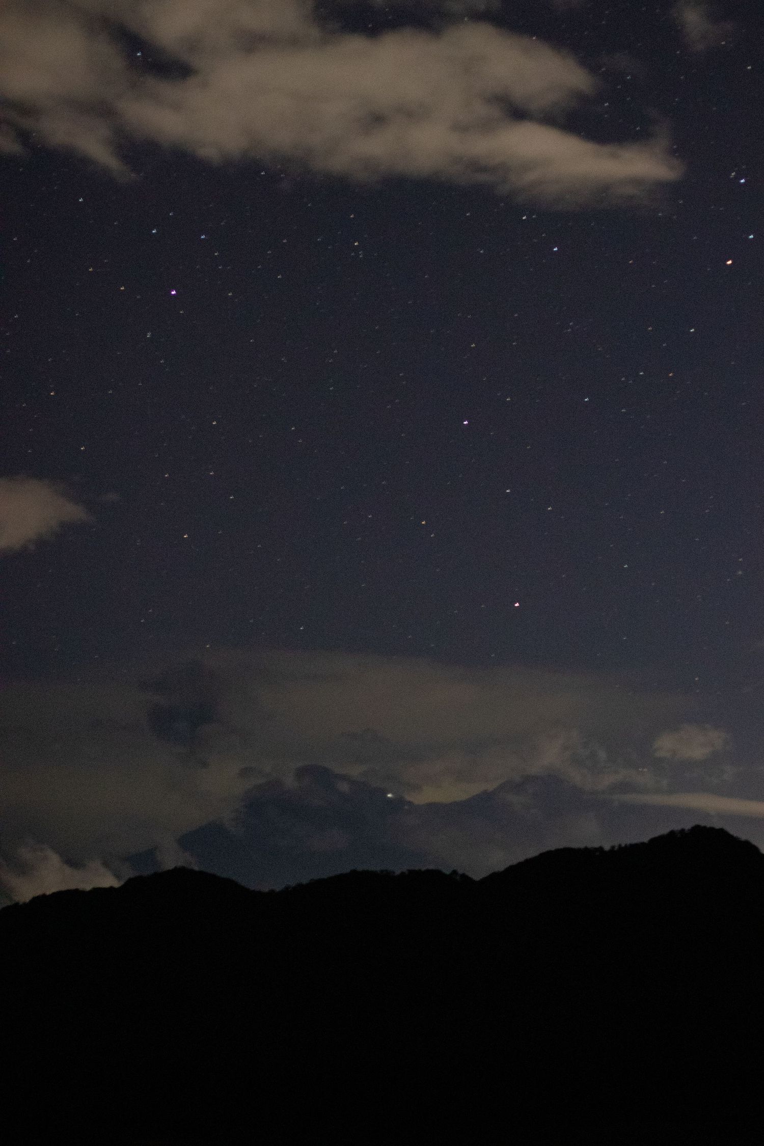 Mountain landscape under a starlit sky with wispy clouds creating a serene nighttime scene.