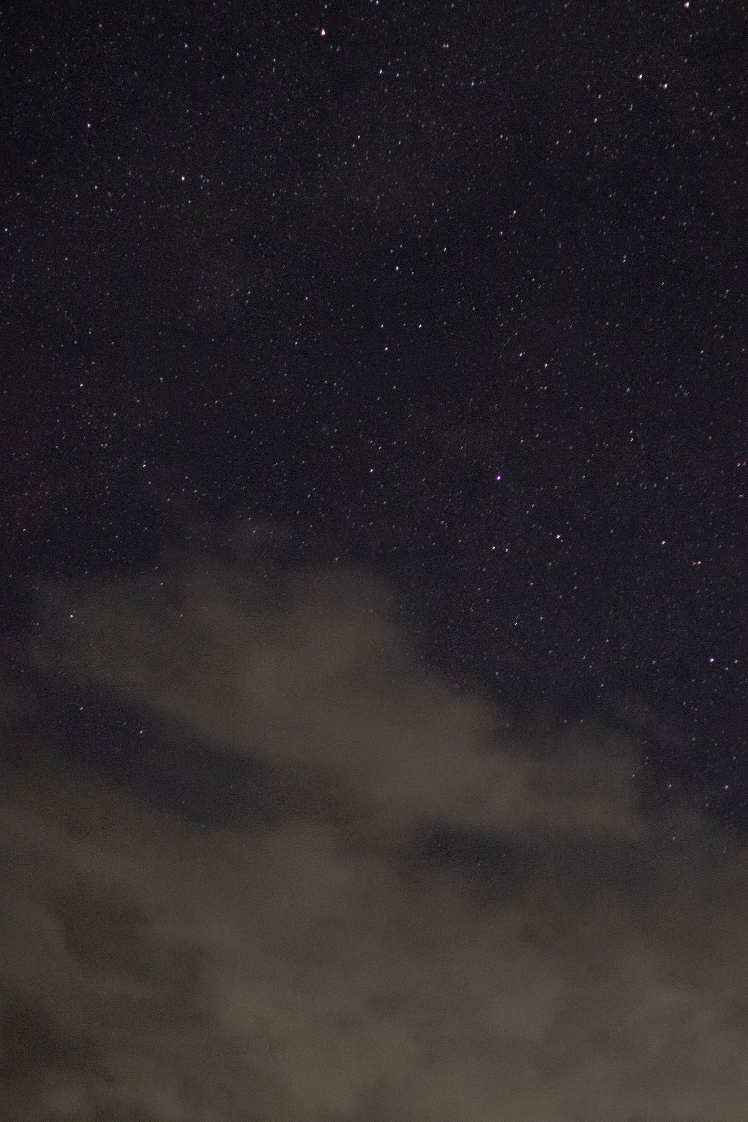 Dark night sky filled with twinkling stars above a mountain range silhouette.