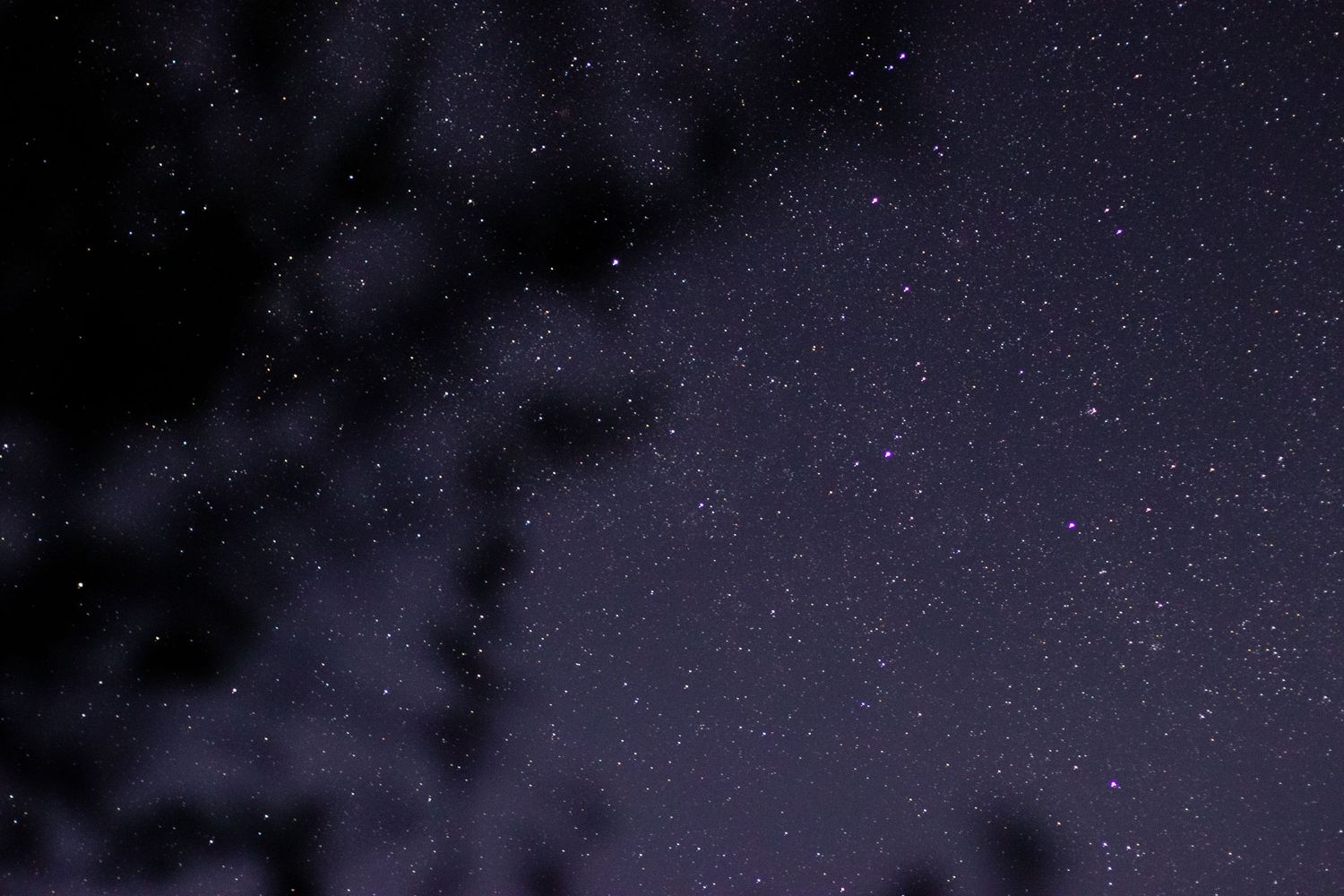 Starry night sky with scattered clouds and mountain silhouettes creating a dramatic natural landscape.