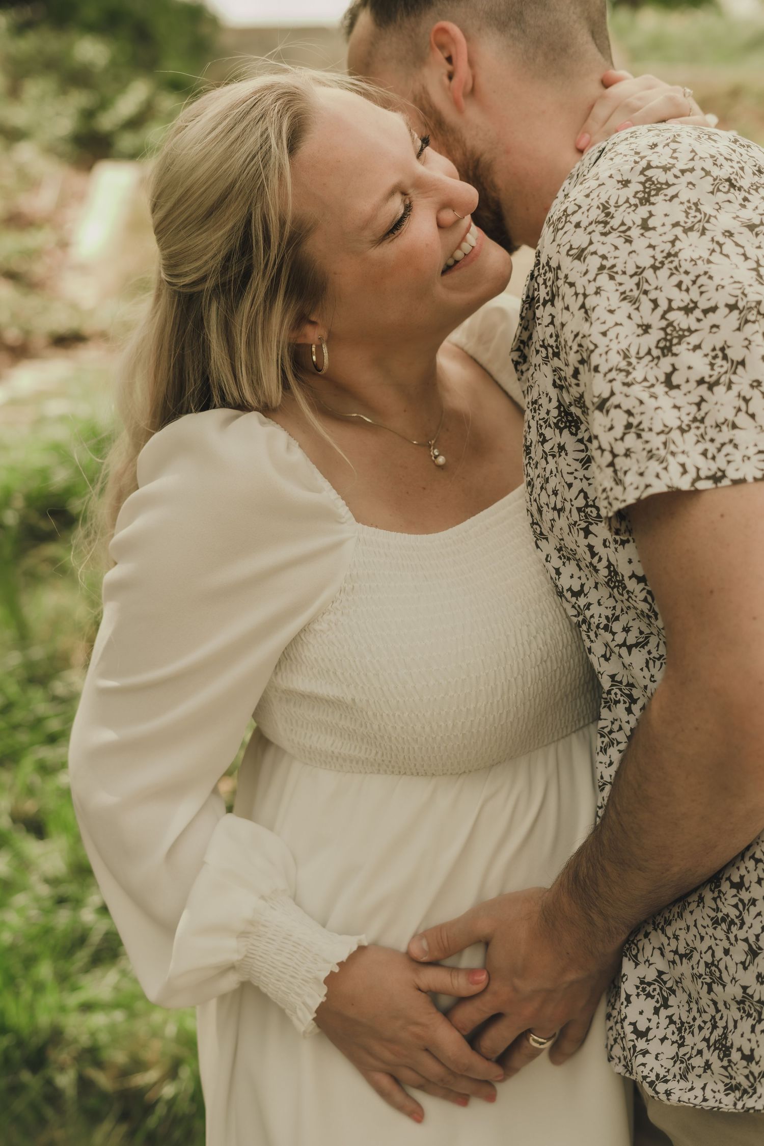 a bride smiling and embracing her husband while he kisses her on the cheek