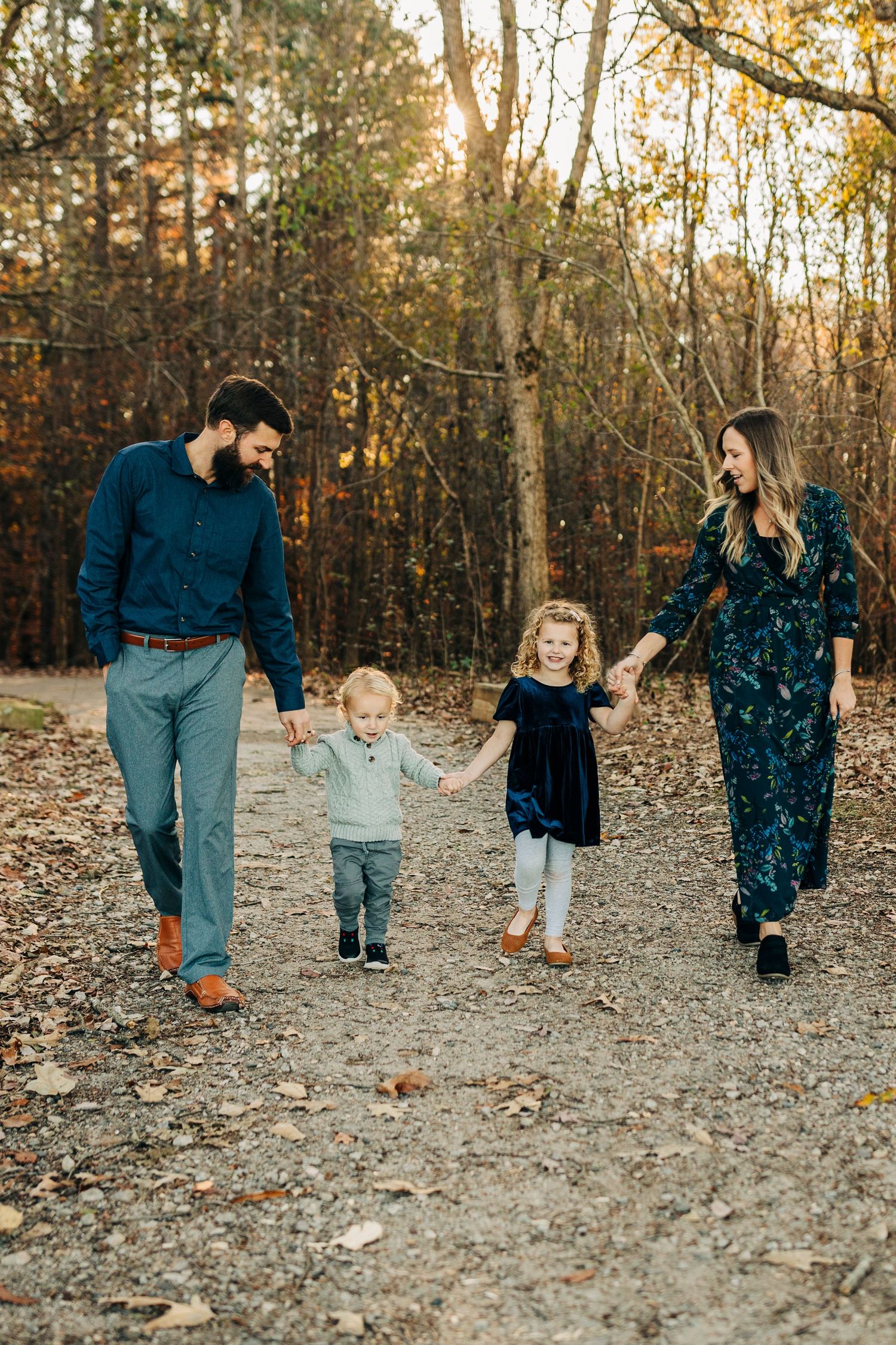 A family walks hand in hand along a forest trail during sunset.